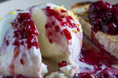 Beyaz mozzarella peyniri, ahududu reçeli ve tabakta bir dilim tam tahıllı ekmek ile servis edilir.