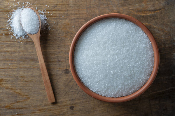White sugar in a clay pot and wooden spoon, top view, close up
