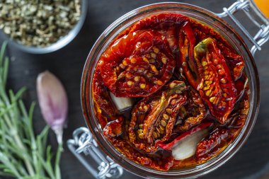 Sarımsaklı, yeşil biberiyeli, güneşte kurutulmuş kırmızı domatesler, ahşap bir masada cam kavanozda zeytinyağı ve baharatlar. Kırsal stil, üst görünüm, kapat