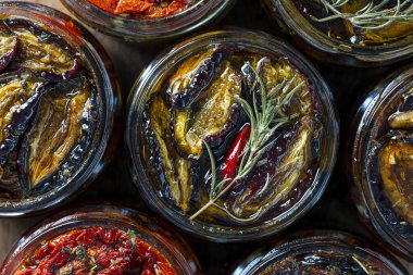 Kurutulmuş kırmızı domates ve sarımsaklı, yeşil biberiyeli erik, kırmızı biber, zeytinyağı ve baharatlar ahşap bir masada cam kavanozda. Kırsal stil, üst görünüm, kapat