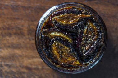 Sarımsaklı güneşte kurutulmuş erikler, yeşil biberiye, kırmızı biber, zeytinyağı ve baharatlar ahşap bir masada cam bir kavanozda. Kırsal stil, üst görünüm, kapat