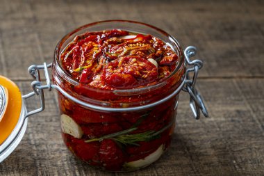 Sarımsaklı, zeytinyağlı ve ahşap bir masada cam kavanozda baharatlı kurutulmuş kırmızı domatesler. Kırsal stil, yakın çekim