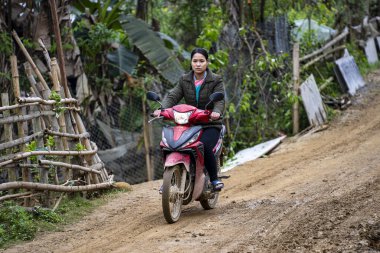 Sapa, Vietnam - Mart 06, 2020: Vietnamlı bir kadın Kuzey Vietnam 'daki Sapa dağ köyünde motosiklet üzerinde toprak bir kır yolunda at sürüyor.