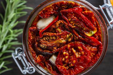 Sarımsaklı, yeşil biberiyeli, güneşte kurutulmuş kırmızı domatesler, ahşap bir masada cam kavanozda zeytinyağı ve baharatlar. Kırsal stil, üst görünüm, kapat