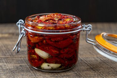 Sarımsaklı, zeytinyağlı ve ahşap bir masada cam kavanozda baharatlı kurutulmuş kırmızı domatesler. Kırsal stil, yakın çekim