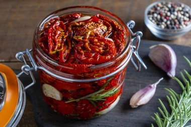 Sarımsaklı, yeşil biberiyeli, güneşte kurutulmuş kırmızı domatesler, ahşap bir masada cam kavanozda zeytinyağı ve baharatlar. Kırsal stil, yakın çekim