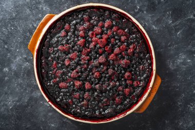 Siyah zemin üzerinde seramik bir tabakta yabanmersinli ve ahudududulu turta.