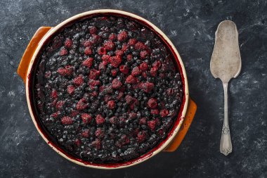 Siyah zemin üzerinde seramik bir tabakta yabanmersinli ve ahudududulu turta.