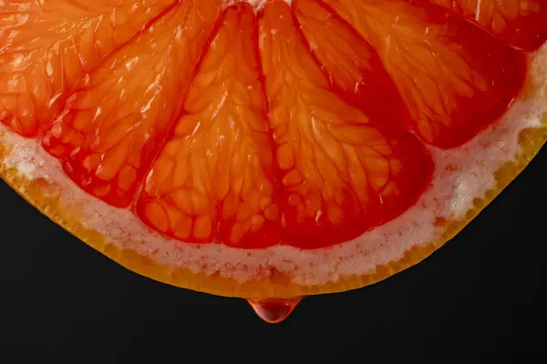 Slice of red grapefruit with juice drops on a black background, macro photography. Texture fresh citrus fruit, close up