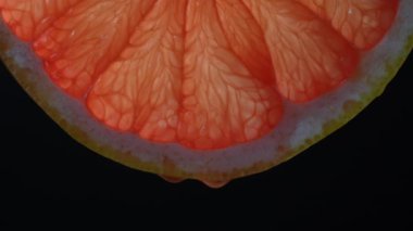 Siyah arka planda meyve suyu damlaları olan kırmızı greyfurt dilimi, makro fotoğraf. Doku taze narenciye, yakın çekim.