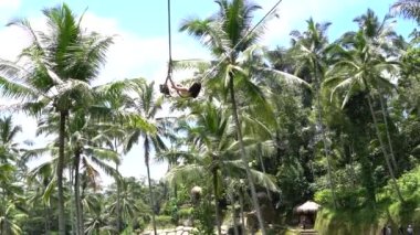 Bali, Indonezya - 11 Mart 2019: Asyalı kız ormanda salıncakta sallanıyor. Ubud, Endonezya yakınlarındaki Bali adasının yağmur ormanlarında sallanan insanlar, ağır çekim