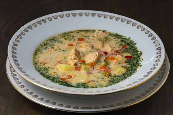 ジャガイモ ニンジン ブロッコリー コショウ タマネギを木製のテーブルの上にセラミックプレートに入れた新鮮なクリーミーなサーモン魚のスープ おいしい夕食はサーモンの魚スープで構成されています — ストック写真