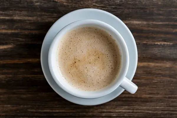 トップビュー 朝の木のテーブルの背景にミルクの泡のコーヒーが付いているカプチーノの白いカップ 閉まる — ストック写真