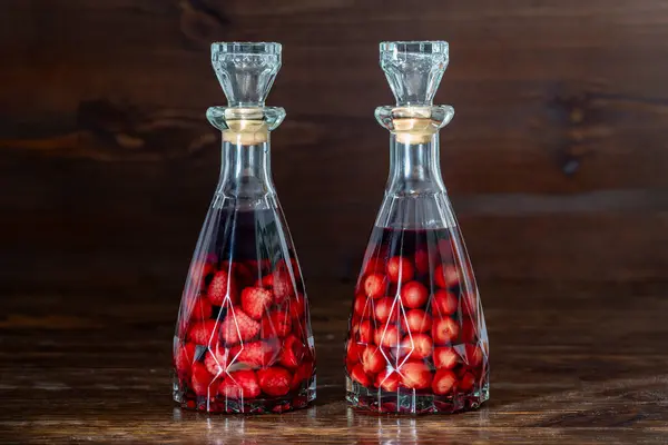 两个玻璃瓶的自制樱桃和覆盆子酒在木制的背景 浆果酒精饮料概念 图库图片