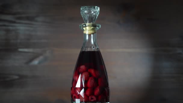 自家製の赤いラズベリーリキュールのガラス瓶は木製の背景に 回転し 閉じます ベリーアルコール飲料コンセプト — ストック動画