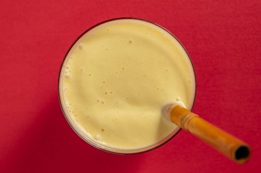Kırmızı arka planda bambu pipetli muzlu mango smoothie, yakın plan, üst manzara