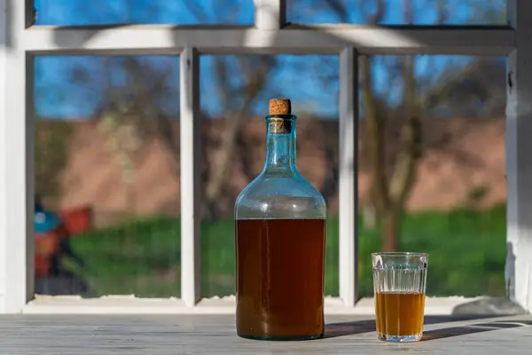 一个温暖的春日 在窗台上用发酵的桦树树液制成的大瓶子 关上了 传统的乌克兰冷大麦在玻璃瓶中喝Kvass 在庭院附近的桌子上喝玻璃杯 — 图库照片