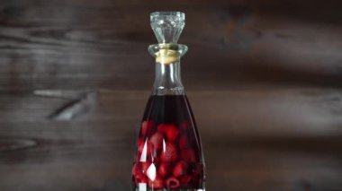 Ahşap arka planda ev yapımı kırmızı ahududu likörü şişesi dönüyor, kapanıyor. Böğürtlen alkollü içki konsepti