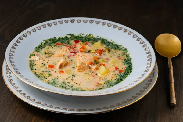 Fresh creamy salmon fish soup with potatoes, carrots, broccoli, peppers and onions in a ceramic plate on a wooden table, close up. A delicious dinner consists of fish soup with salmon