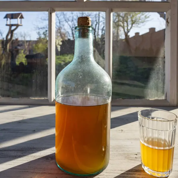 一个温暖的春日 在窗台上用发酵的桦树树液制成的大瓶子 关上了 传统的乌克兰冷大麦在玻璃瓶中喝Kvass 在庭院附近的桌子上喝玻璃杯 免版税图库图片