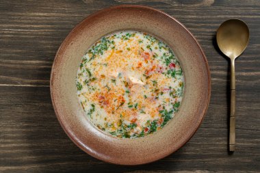 Tahta bir masada seramik tabakta patates, havuç, biber ve soğanlı taze kremalı somon balığı çorbası, yakın plan, üst manzara. Lezzetli bir akşam yemeği somonlu balık çorbasından oluşur.