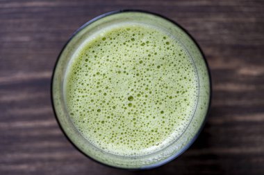 Bir bardak yeşil smoothie, yakın çekim, üst manzara. Muz, dereotu, maydanoz ve avokadodan yapılan sağlıklı organik içecek. Yeşil bir içeceğin yüzeyinde köpükler ve kabarcıklar.