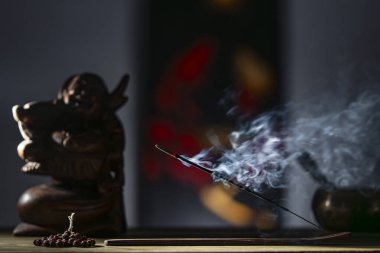 Çubuk tutacağındaki Asya tütsü çubuğu koyu arka planda dumanla yanıyor. Yaklaş. Meditasyon, yoga, kişisel gelişim ve ses terapisi kavramı