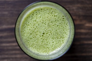 Bir bardak yeşil smoothie, yakın çekim, üst manzara. Muz, dereotu, maydanoz ve avokadodan yapılan sağlıklı organik içecek. Yeşil bir içeceğin yüzeyinde köpükler ve kabarcıklar.