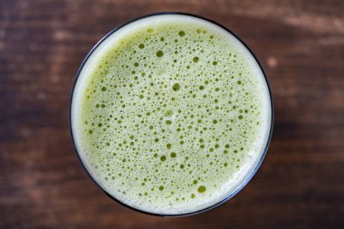 Bir bardak yeşil smoothie, yakın çekim, üst manzara. Muz, dereotu, maydanoz ve avokadodan yapılan sağlıklı organik içecek. Yeşil bir içeceğin yüzeyinde köpükler ve kabarcıklar.