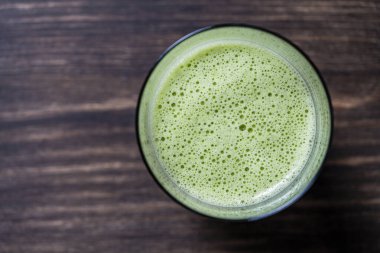 Bir bardak yeşil smoothie, yakın çekim, üst görüş, kopyalama alanı. Muz, dereotu, maydanoz ve avokadodan yapılan sağlıklı organik içecek. Yeşil bir içeceğin yüzeyinde köpükler ve kabarcıklar.