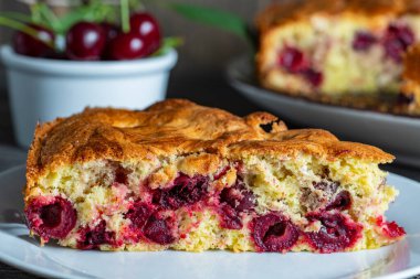 Beyaz tabakta vişneli turta ve ahşap bir masada taze kirazlar. Lezzetli ev yapımı kirazlı Amerikan pastası. Kahvaltıda tatlı