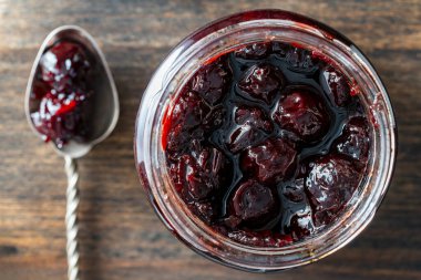 Cam kavanoz kırmızı kiraz reçeli, ahşap arka planda kaşık, üst manzara, kapat