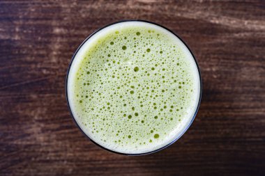 Bir bardak yeşil smoothie, yakın çekim, üst manzara. Muz, dereotu, maydanoz ve avokadodan yapılan sağlıklı organik içecek. Yeşil bir içeceğin yüzeyinde köpükler ve kabarcıklar.