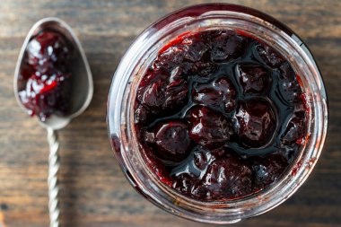Cam kavanoz kırmızı kiraz reçeli, ahşap arka planda kaşık, üst manzara, kapat