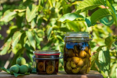Cam kavanozdaki alkolün içinde dilimlenmemiş ceviz, ev yapımı tentürü hazırlamak için, yakın çekim. Yaz bahçesindeki masada cam bir kavanozda yeşil ceviz tentürü.