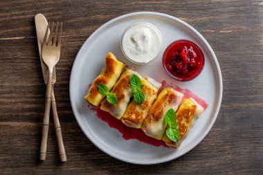 Kızarmış krep, süzme peynir ve kirazla doldurulmuş, tabakta tatlı, yakın plan, üst manzara. Ev yapımı pişirme. Kahvaltı için nefis fast food. Ekşi kremalı ve reçelli krep.