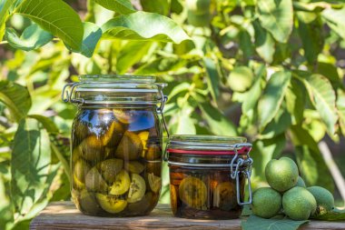 Cam kavanozdaki alkolün içinde dilimlenmemiş ceviz, ev yapımı tentürü hazırlamak için, yakın çekim. Yaz bahçesindeki masada cam bir kavanozda yeşil ceviz tentürü.