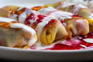 Kızarmış krep, süzme peynir ve kirazla doldurulmuş, tabakta tatlı, kapat. Ev yapımı pişirme. Kahvaltı için nefis fast food. Ekşi kremalı ve reçelli krep.