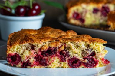 Beyaz tabakta vişneli turta ve ahşap bir masada taze kirazlar. Lezzetli ev yapımı kirazlı Amerikan pastası. Kahvaltıda tatlı