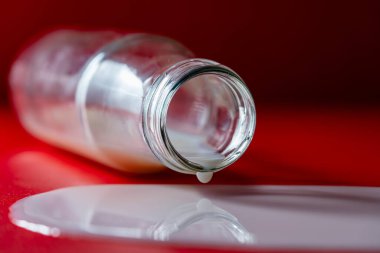 Glass bottle with spilled milk on a red background, close up clipart