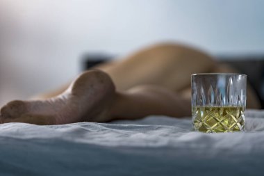 Bir bardak alkol ve yatakta uyuyan sarhoş çıplak kız. Sorunlu kadın ve alkol kavramı. Partiden sonraki sabah. Bulanık odak