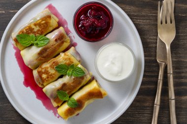 Kızarmış krep, süzme peynir ve kirazla doldurulmuş, tabakta tatlı, yakın plan, üst manzara. Ev yapımı pişirme. Kahvaltı için nefis fast food. Ekşi kremalı ve reçelli krep.