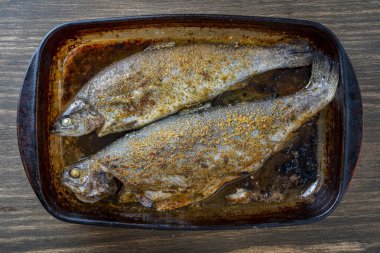 Lezzetli fırında iki alabalık ve cam bir tencerede baharat, yakın çekim, üst manzara.