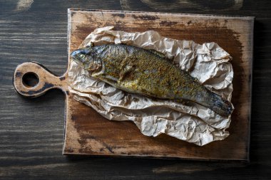 Lezzetli fırında bir alabalık, kesme tahtasının üzerinde baharatlar, yakın çekim, üst manzara.