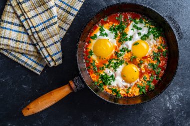 Shakshuka kahvaltıda kızartma tavasında, kapat. Kızarmış yumurta, soğan, dolma biber, kırmızı domates ve maydanoz karışımından yapılmış ev yapımı shakshuka dökme demir tavada, üst görünümde.