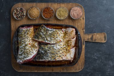 Baharatlı sazan balığı filetosu, baharat ve şifalı cam fırın tabağı, kesme tahtası, kapat, üst manzara.