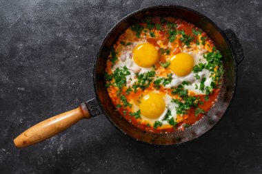 Shakshuka kahvaltıda kızartma tavasında, kapat. Kızarmış yumurta, soğan, dolma biber, kırmızı domates ve maydanoz karışımından yapılmış ev yapımı shakshuka dökme demir tavada, üst görünümde.
