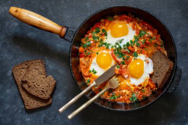 Shakshuka kahvaltıda kızartma tavasında, kapat. Kızarmış yumurta, soğan, dolma biber, kırmızı domates ve maydanoz karışımından yapılmış ev yapımı shakshuka dökme demir tavada, üst görünümde.