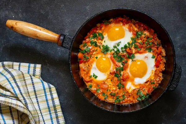 Shakshuka kahvaltıda kızartma tavasında, kapat. Kızarmış yumurta, soğan, dolma biber, kırmızı domates ve maydanoz karışımından yapılmış ev yapımı shakshuka dökme demir tavada, üst görünümde.