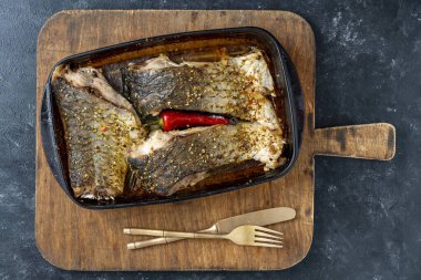Kırmızı biberli fırında sazan balığı filetosu ve doğrama tahtasındaki cam fırın kabında baharatlar.